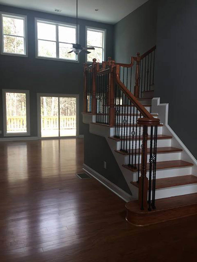 Wood staircase with black metal railings, light-colored flooring, sliding glass door, and large window in modern home interior