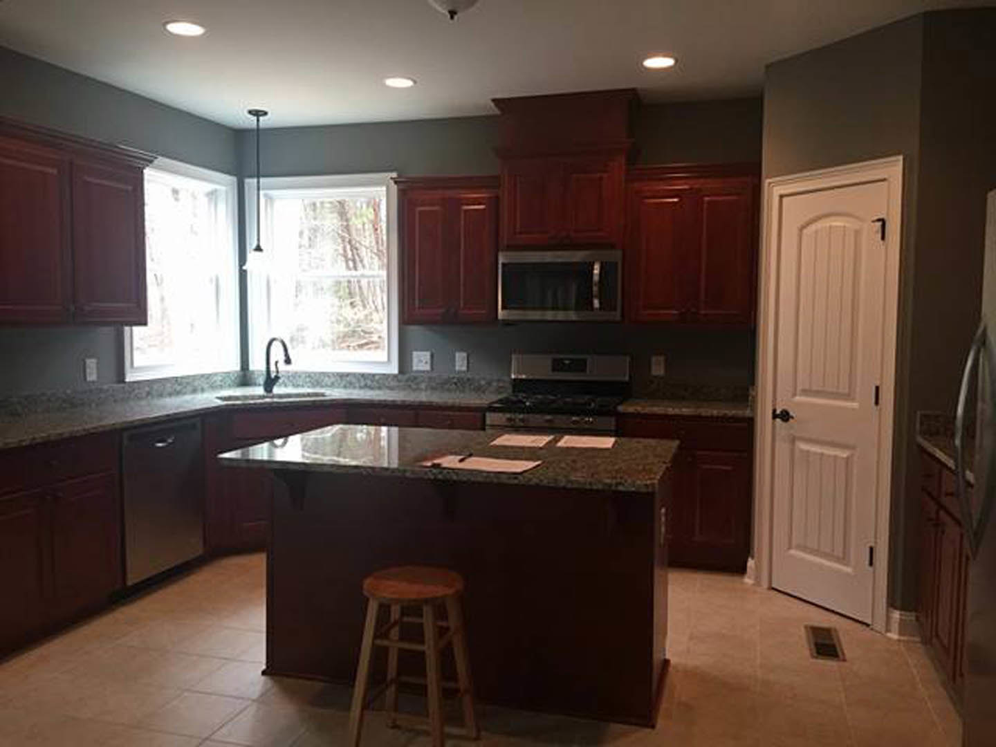Modern kitchen with light wood cabinetry, white quartz countertops, built-in stainless steel appliances, a bar area with a single wooden stool, and a white door with black handle