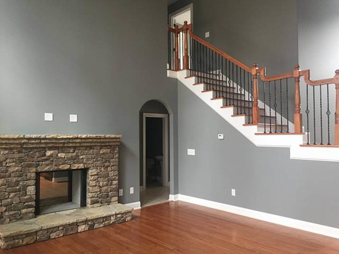 Wood staircase with matching railings, stone fireplace with glass door, hardwood floors, stone ledge, and nearby door and window in a custom home interior