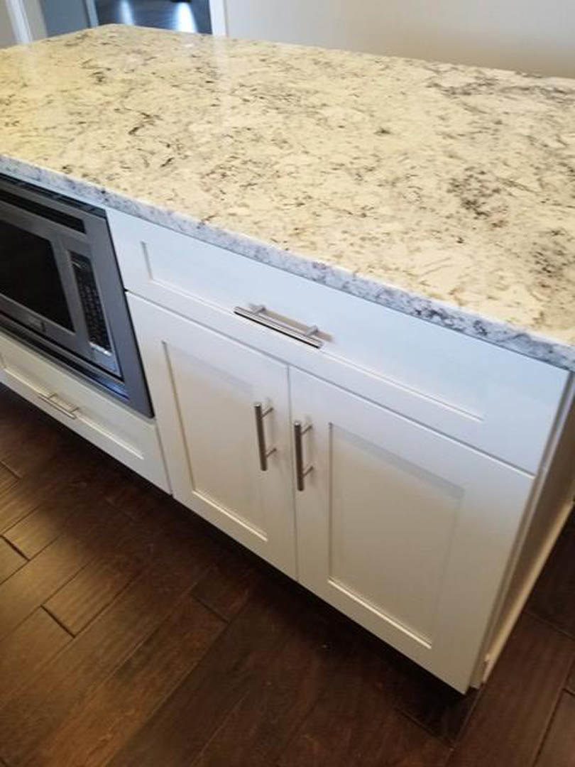 White kitchen countertop with black speckled marble, built-in stainless steel microwave, and white cabinetry