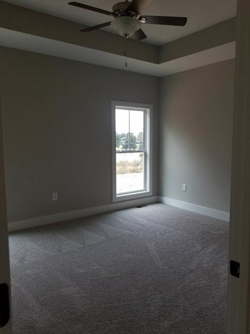 Neutral-toned room featuring a large window, plaster walls, wood flooring, and a ceiling fan with integrated light fixture.