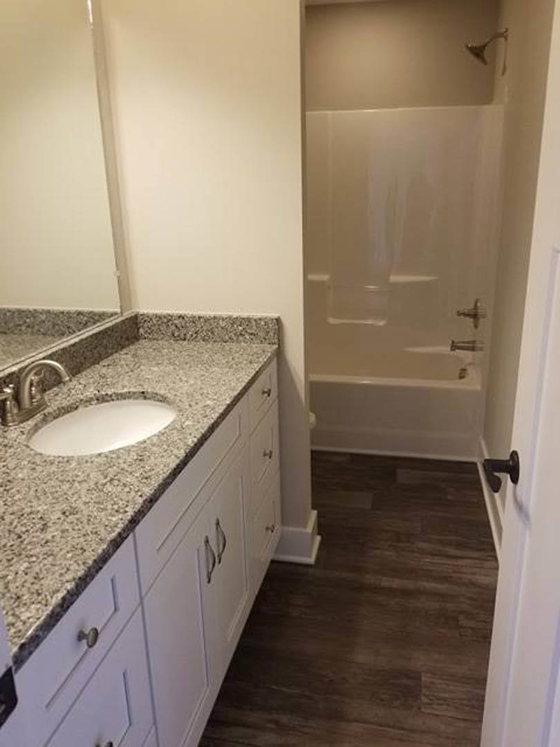 Modern bathroom with white ceramic sink, chrome faucet, glass-enclosed shower, light wood vanity, large wall mirror, and neutral tile flooring