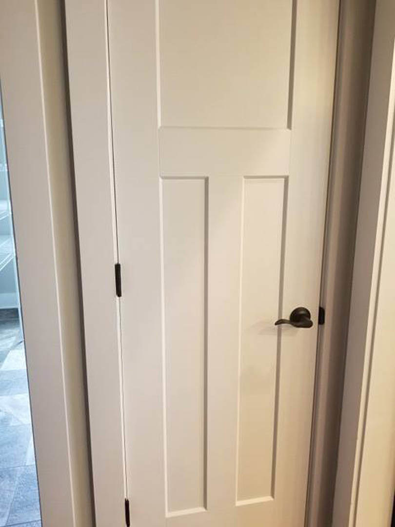 White paneled door with matte black lever handle set in a white wall