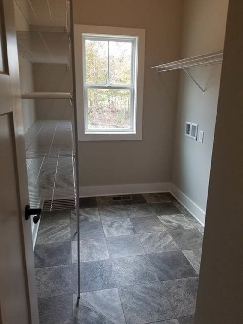 Bright room featuring a large window overlooking trees, grey tile flooring, built-in shelves, and white plaster walls.