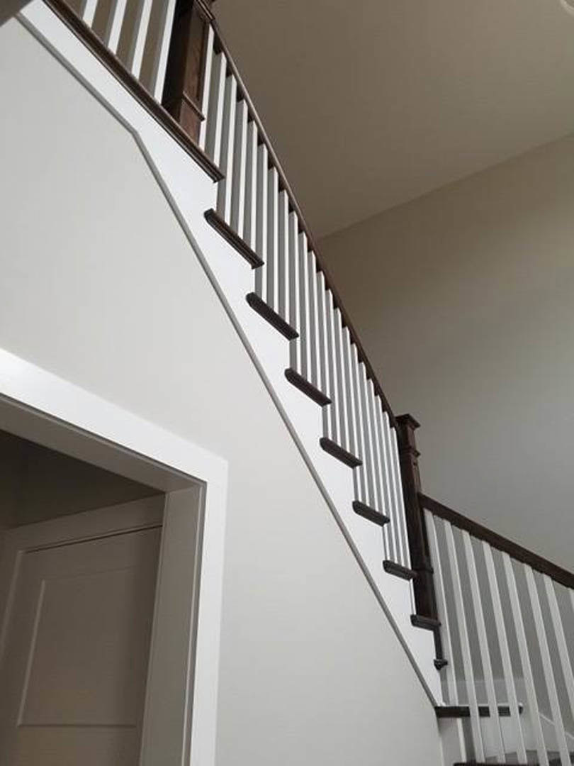 White-painted staircase with matching railings, white door and door frame, smooth white walls, and decorative molding in a bright indoor space
