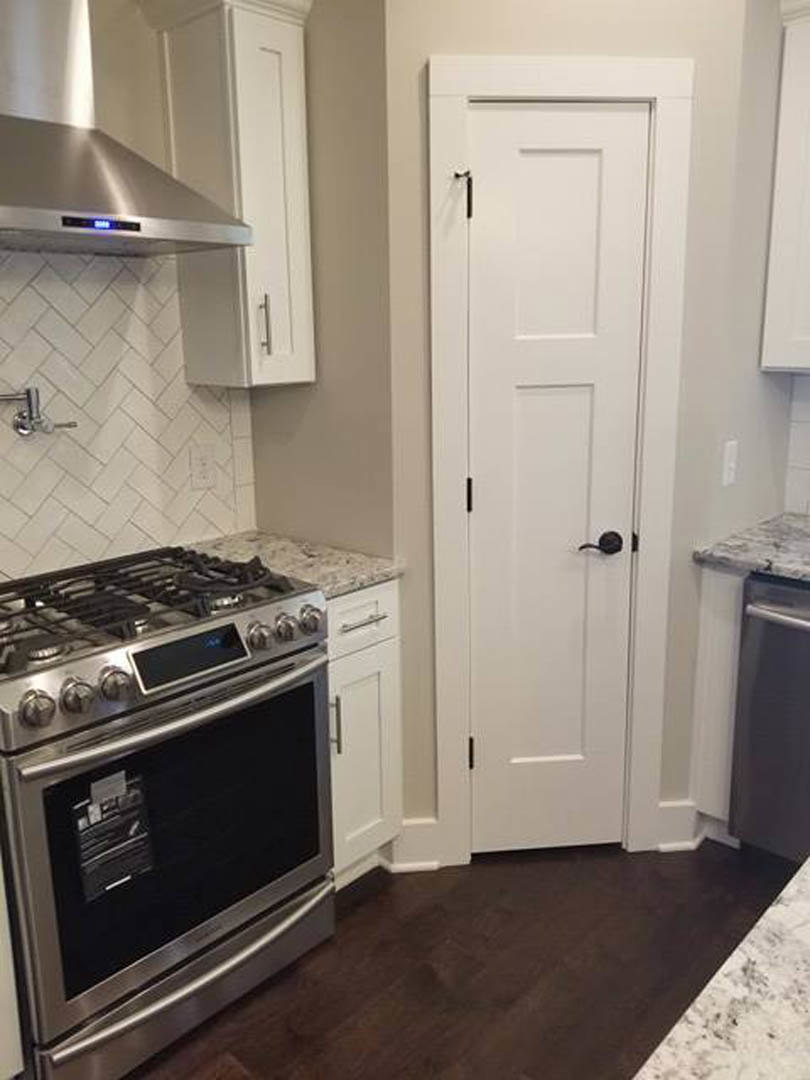 White shaker cabinets, stainless steel stove, marble countertop, dark wood flooring, white door with black handle