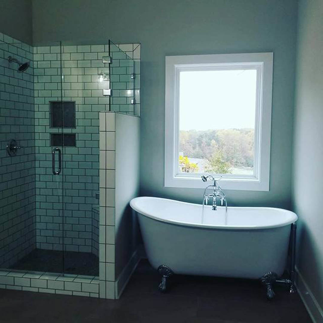 White tiled bathroom featuring a freestanding soaking tub with chrome faucet, glass-enclosed shower, large window, and modern sink with polished fixtures