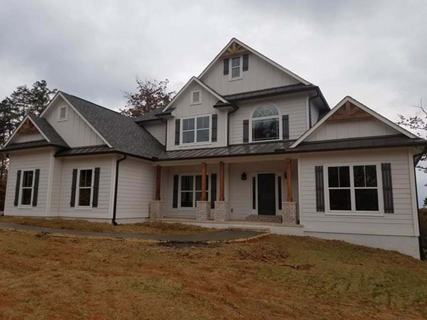 Two-story home with light siding, large windows, covered porch, wet concrete walkway, and green lawn in front