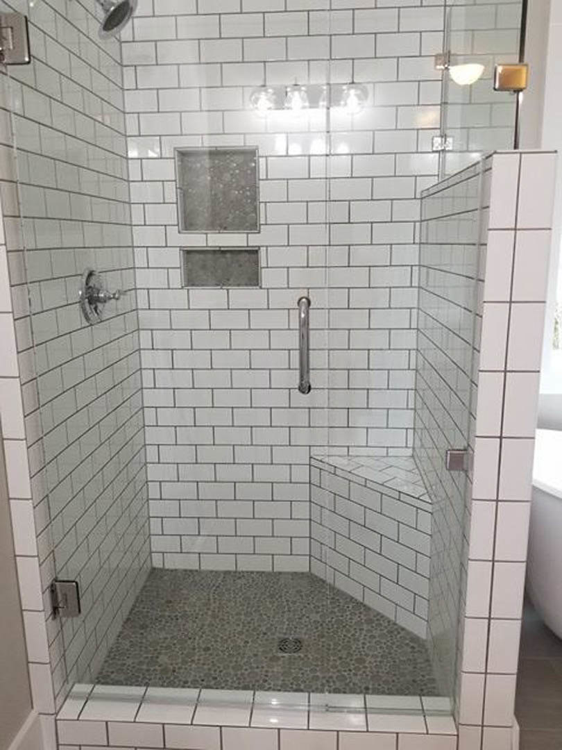 Walk-in shower featuring gray tile floor, matching tiled walls, glass enclosure, chrome fixtures, and built-in niche for bathroom accessories