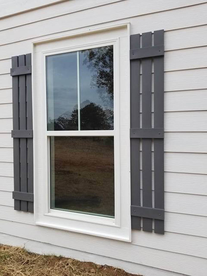 White-framed window with gray shutters set in light-colored siding, partial view of a nearby fence