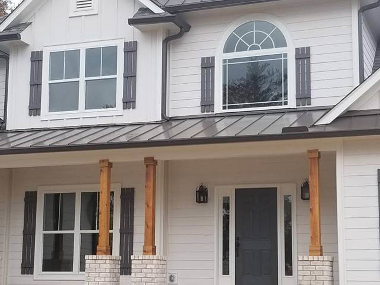 Gray brick pillars supporting covered porch, black front door, white-framed sash window, light gray siding, rain gutter along roofline.
