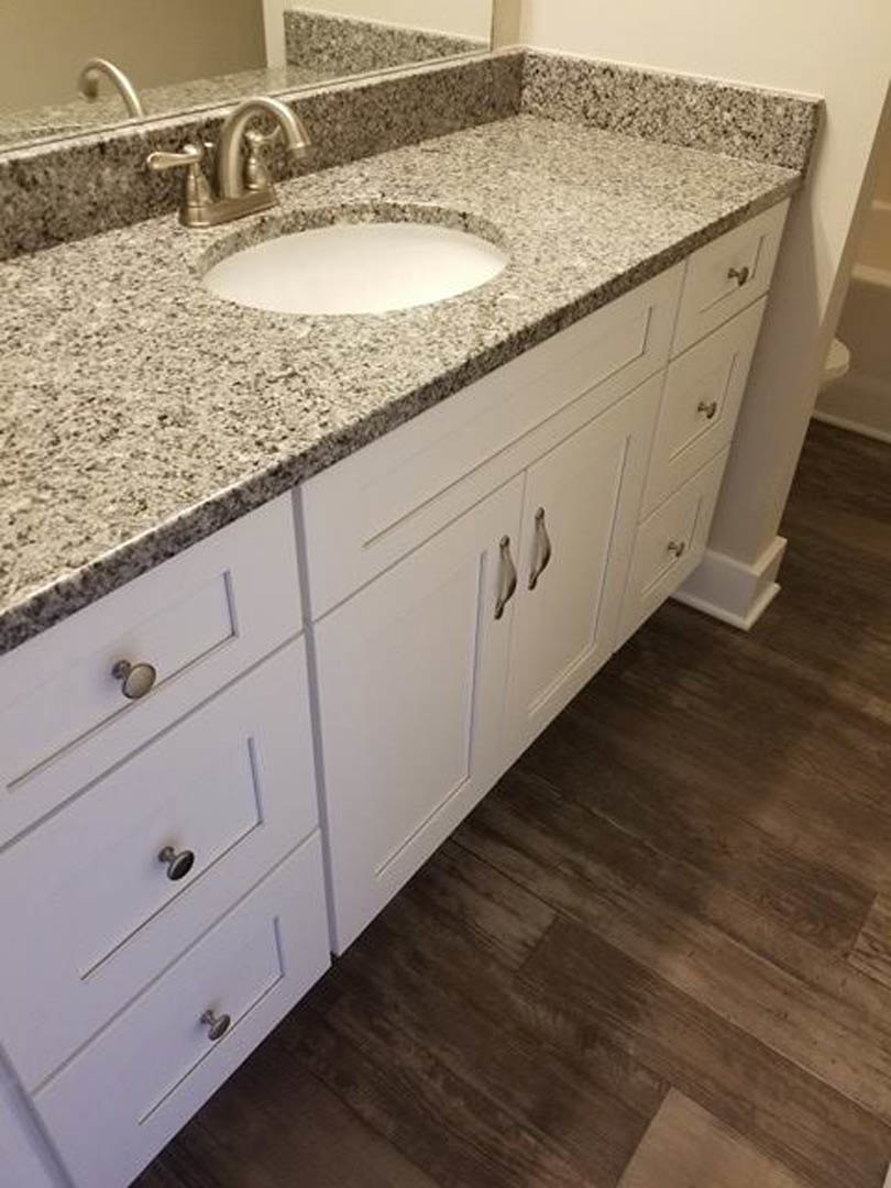 Marble bathroom countertop with chrome faucet, white cabinetry, and tiled backsplash