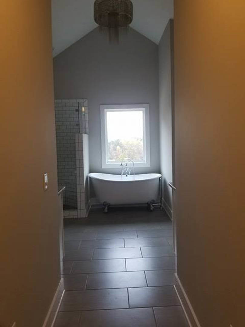 Bathroom with freestanding tub beneath a white-framed window, white tile walls with border, dark tiled floor, and ceiling light fixture