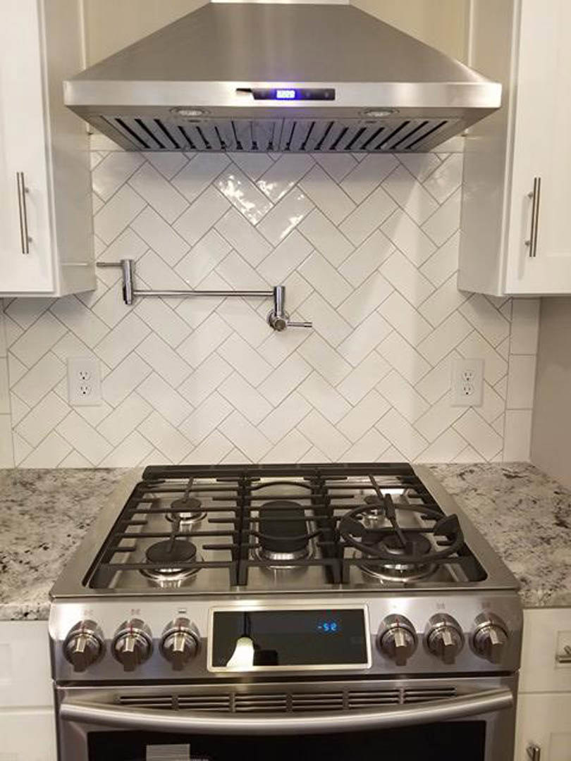 Stainless steel gas stove with digital display beneath a modern range hood, surrounded by white cabinetry and quartz countertops in a contemporary kitchen.