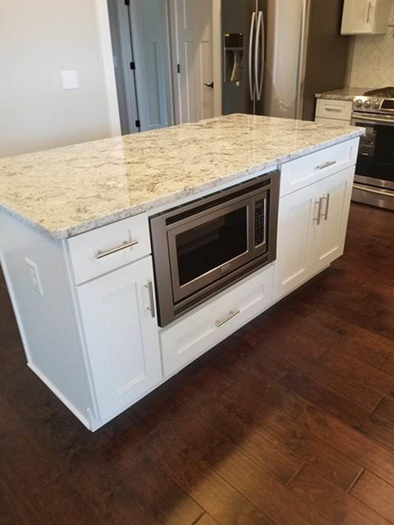Marble kitchen island with built-in microwave, white cabinetry, and light wood flooring