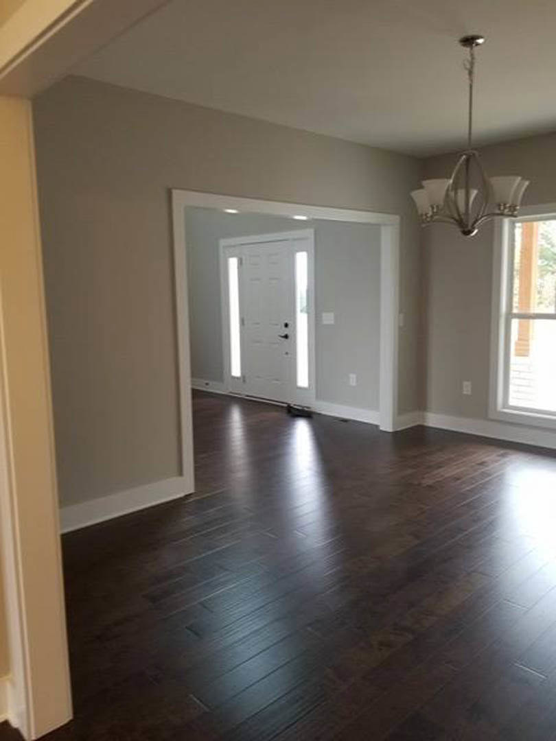 White door with black handle, dark hardwood floor with white baseboards, white-framed window, ceiling light fixture, smooth white walls