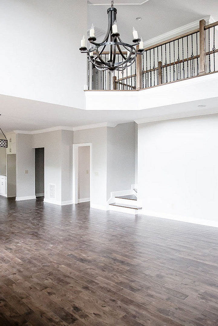 Spacious room with hardwood flooring, white plaster walls, metal-railed staircase, and candle-style chandelier hanging from the ceiling