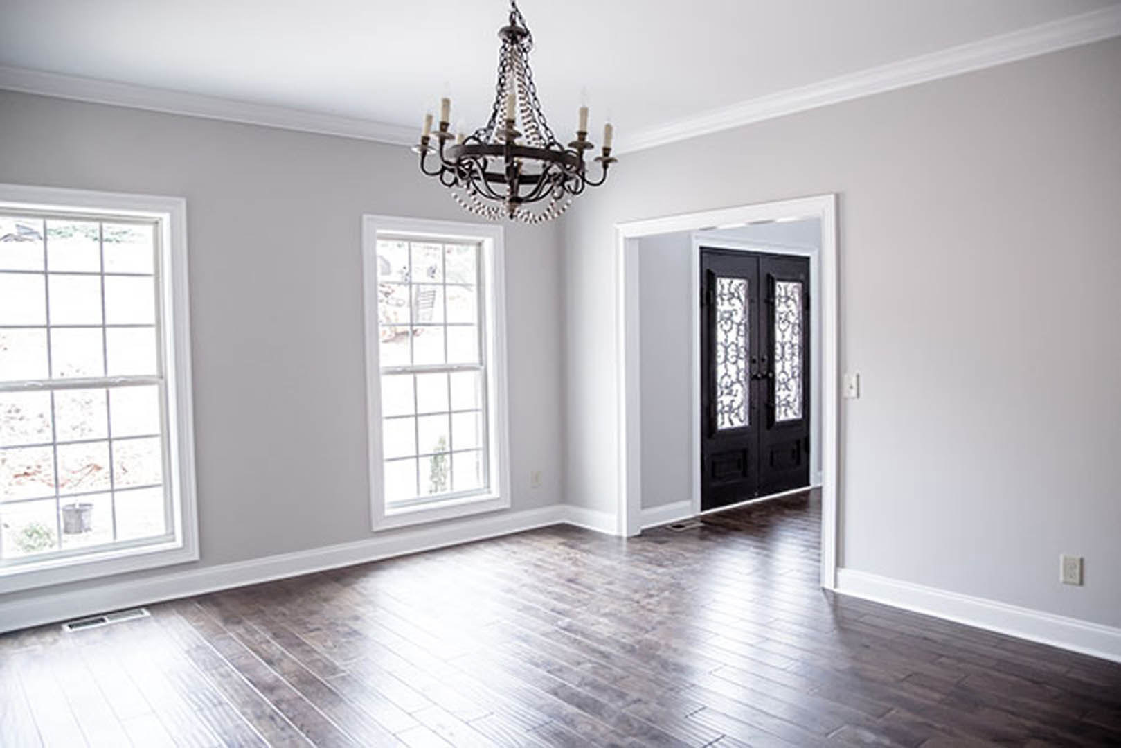 Chandelier hanging from ceiling, wood flooring, white plaster walls, decorative molding, doorway leading to adjacent room