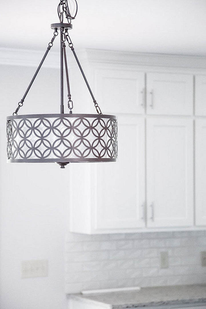 White-shaded pendant light fixture above kitchen island with wood cabinetry and stainless steel appliances