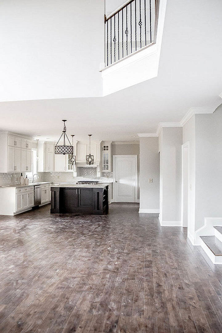 Open-concept kitchen and dining area featuring wood flooring, white walls, sleek cabinetry, a white door with silver handle, and a prominent white staircase with metal railing.