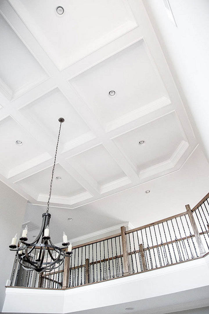 Chandelier hanging from plaster ceiling with decorative molding, staircase with handrail, daylight streaming into spacious interior with neutral walls