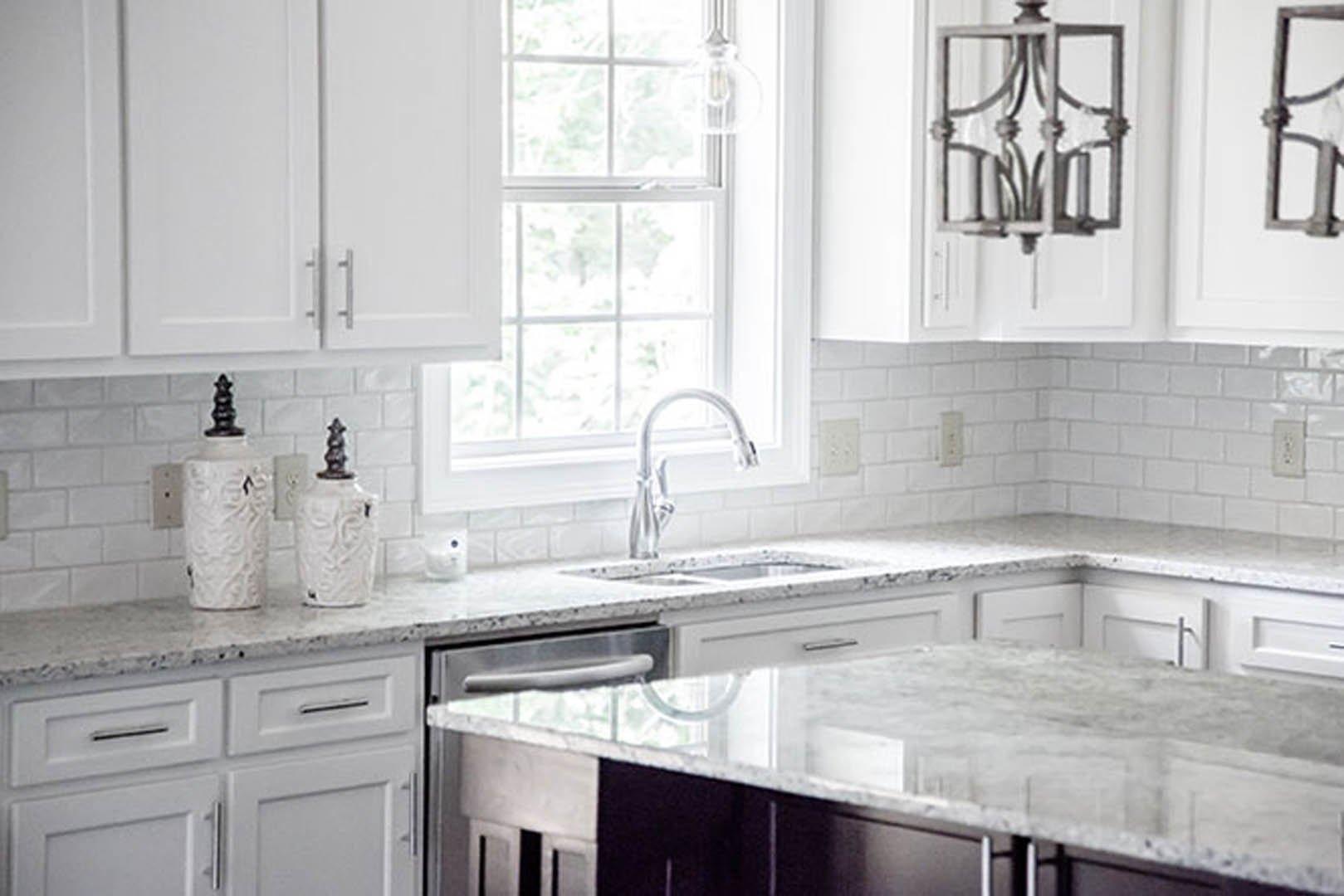 Kitchen featuring white shaker cabinets, marble countertops, stainless steel sink with chrome faucet, and light tile backsplash