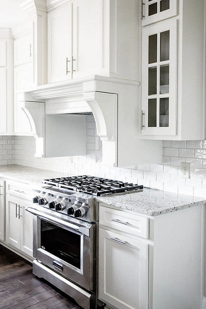 White kitchen with shaker-style cabinets, stainless steel gas stove and oven, light quartz countertops, and subway tile backsplash