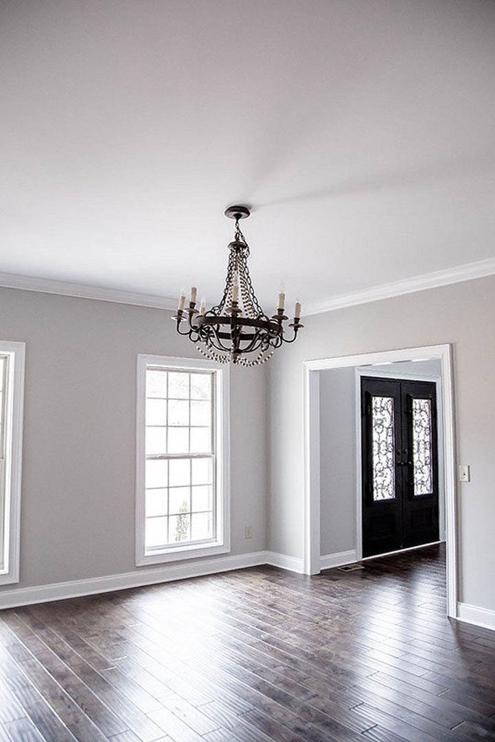 Chandelier with candle-style lights hanging from ceiling above wooden laminate floor, double doors with molding, plaster walls, and window in custom home interior.