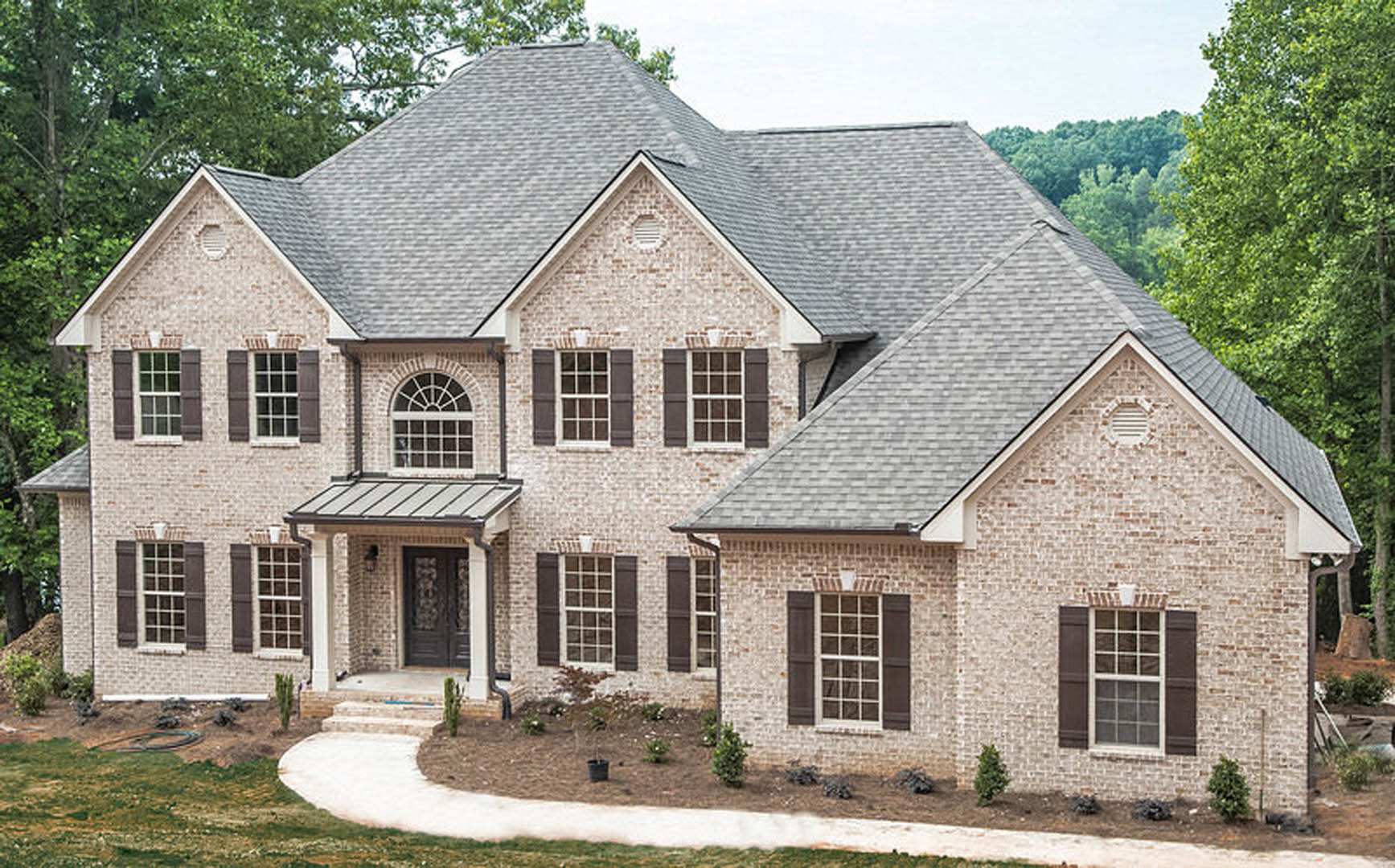 Red brick house with white-trimmed multi-pane windows, paved driveway, mature trees in the background