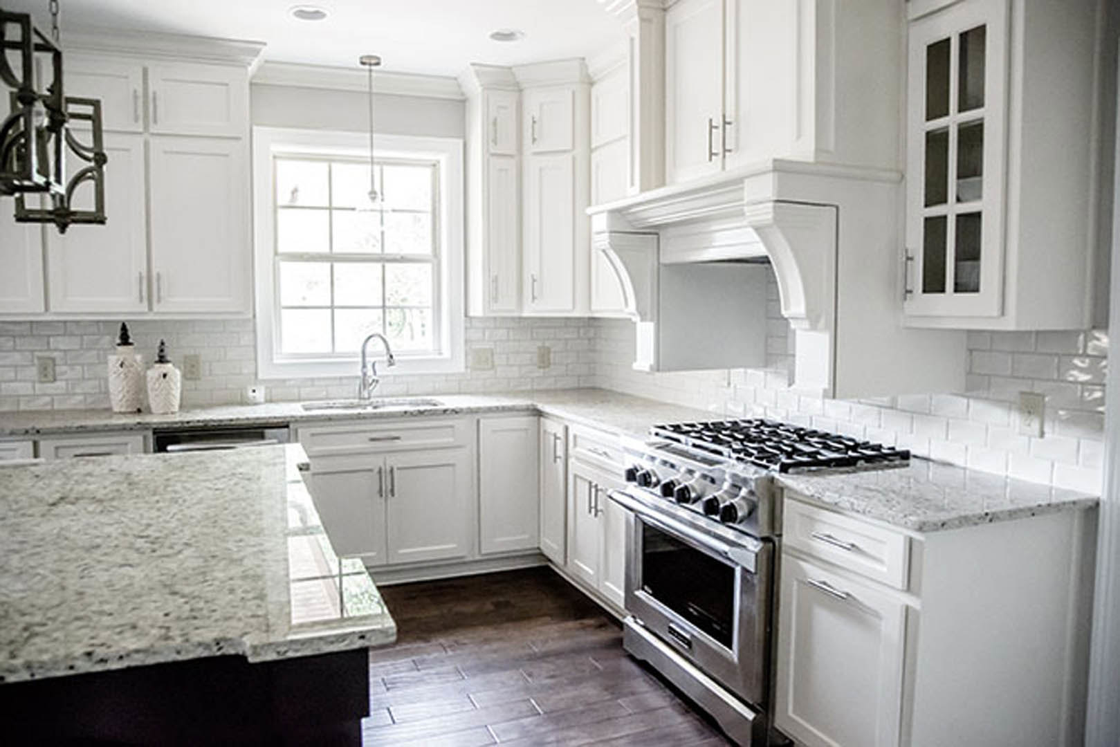 White kitchen cabinets paired with marble countertops, stainless steel oven, and smooth white backsplash