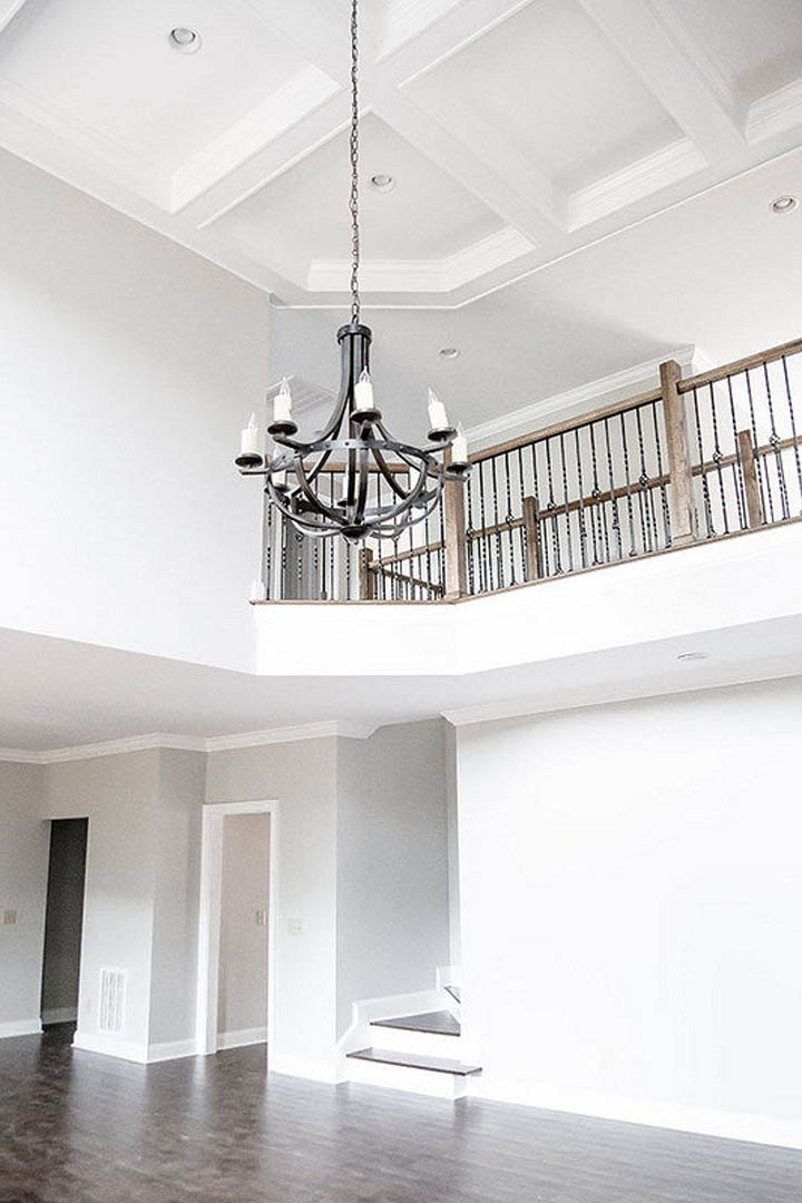 Chandelier with glass accents hangs from white plaster ceiling above hardwood floor, surrounded by neutral walls and modern track lighting.