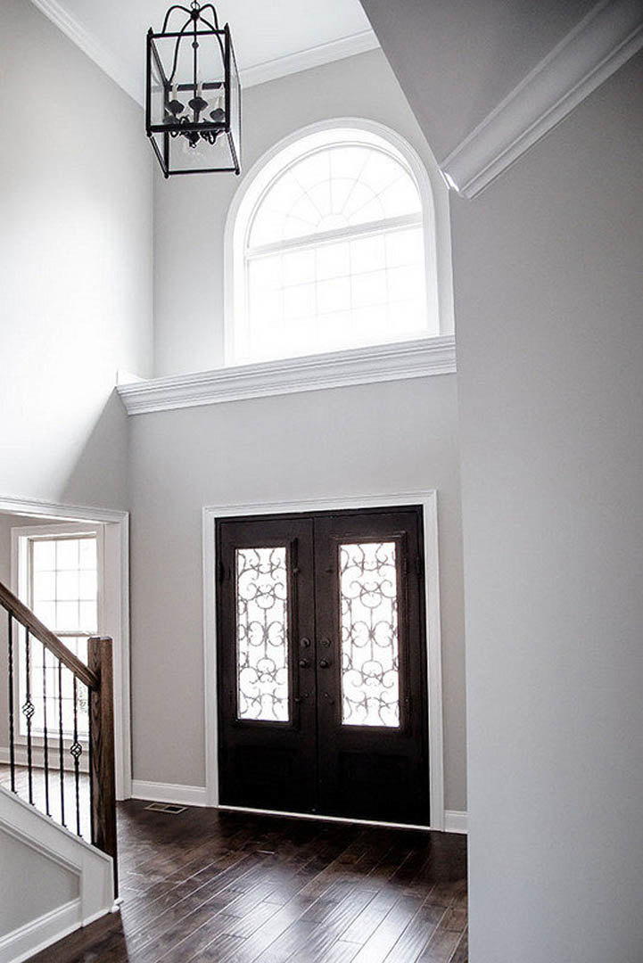 Wide double doors with glass panels set in a white plaster wall, crown molding above, hardwood floors below, and natural daylight streaming through adjacent windows.