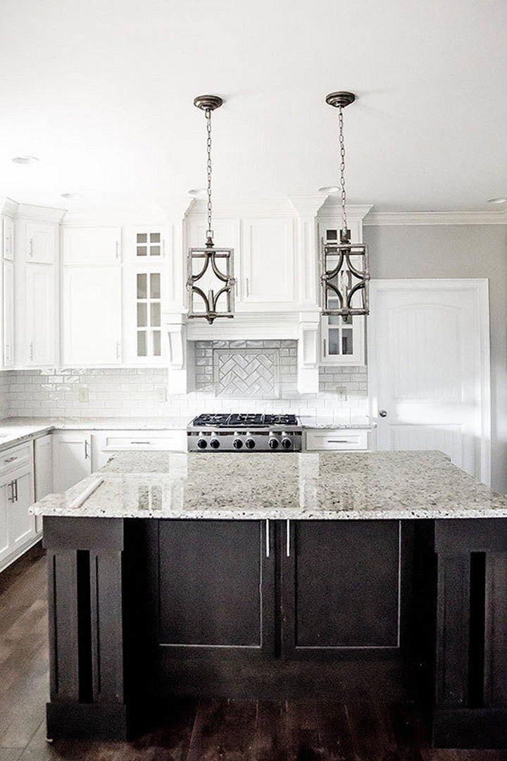 Marble island with waterfall edge, stainless steel stove, grey cabinetry, undermount sink, chrome faucet, and light tile backsplash