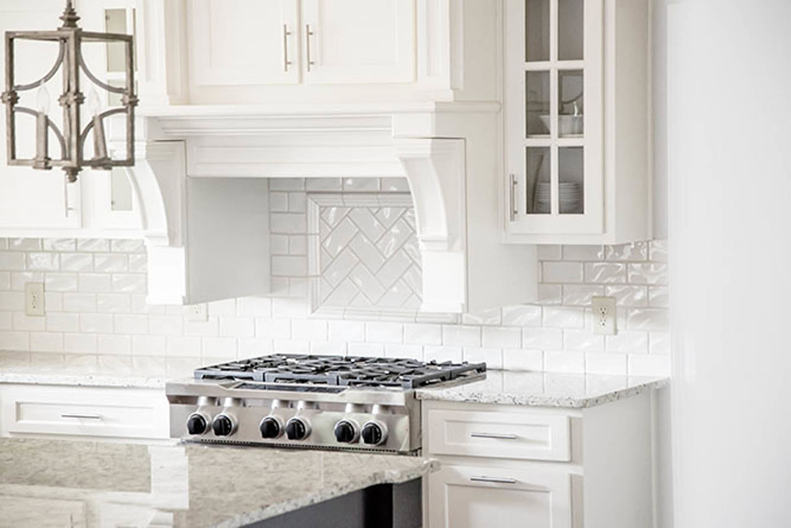 White shaker cabinets, stainless steel gas stove, quartz countertops, subway tile backsplash, wall outlet visible near cooking area