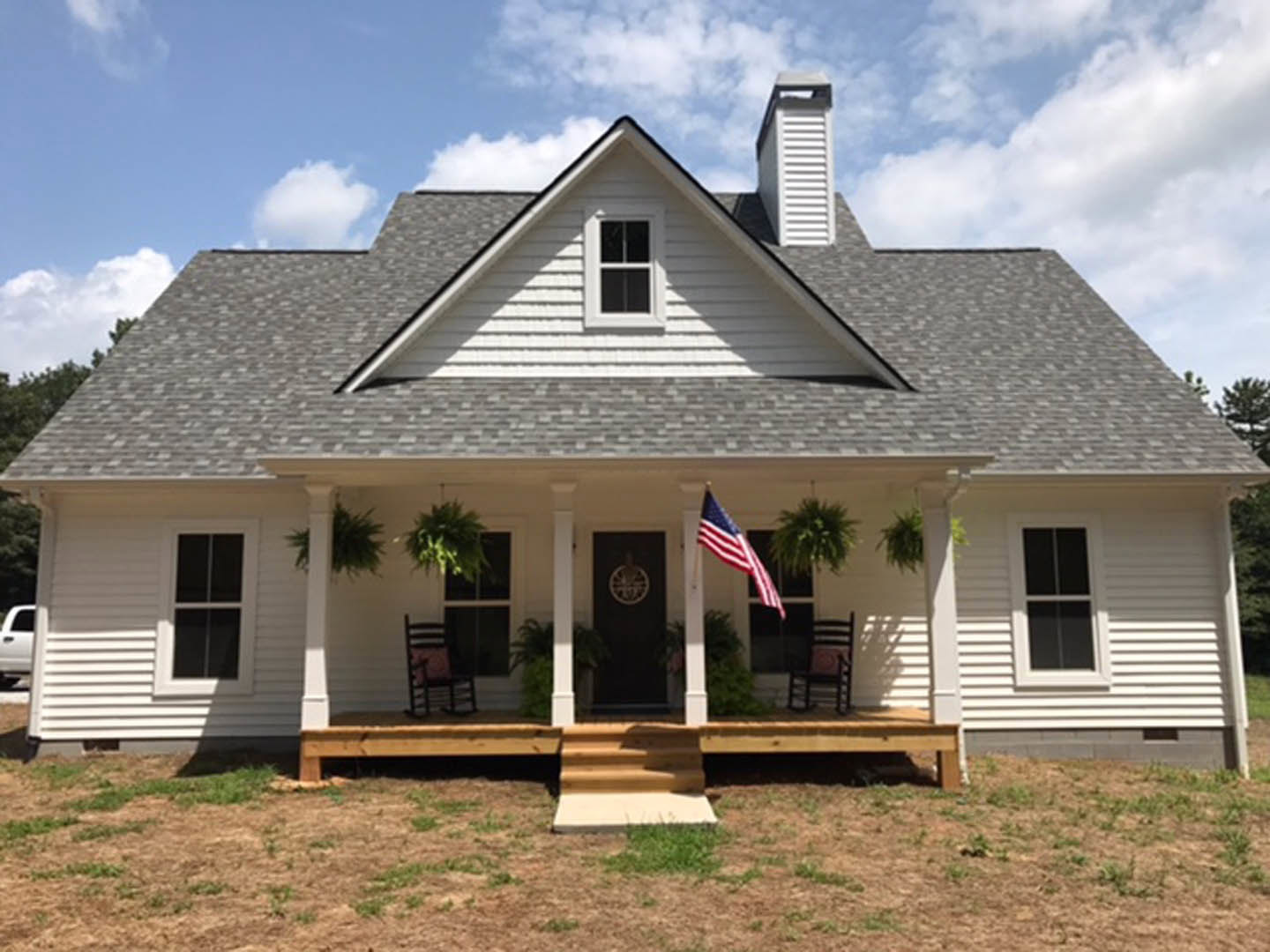 White clapboard house with covered porch, American flag mounted near entrance, multi-pane windows with white trim, Robert Frost Farm visible in background, cloudy sky overhead.
