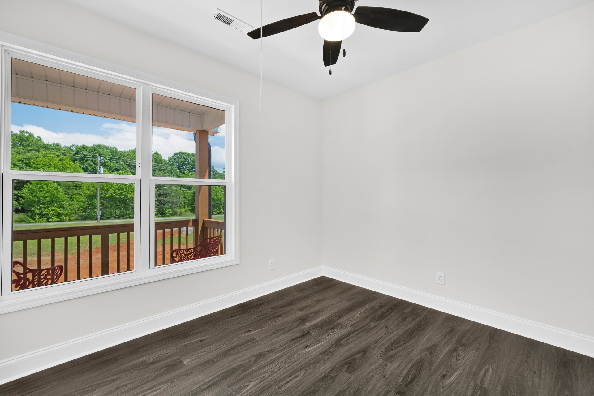 Wood-floored room featuring a ceiling fan with light, large window, and partial view of a red fence outside