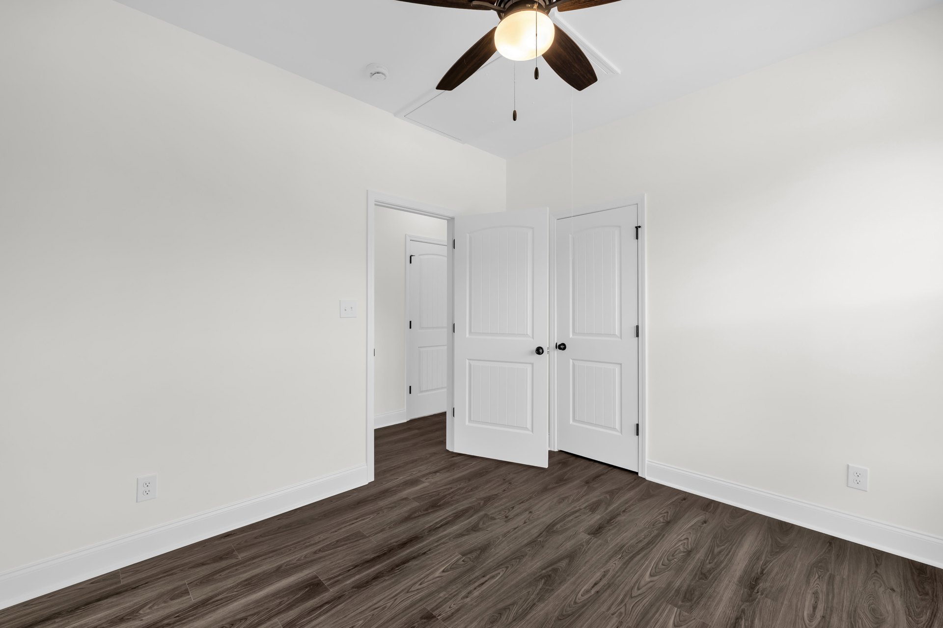 White-walled room with wood flooring, white door featuring black knob, ceiling fan with integrated light fixture