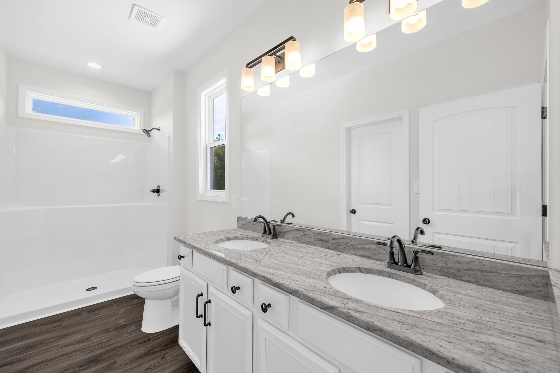 Bathroom featuring white cabinetry, marble countertops, undermount sink with chrome faucet, white toilet, curved-top white door, and ceiling-mounted light fixture.