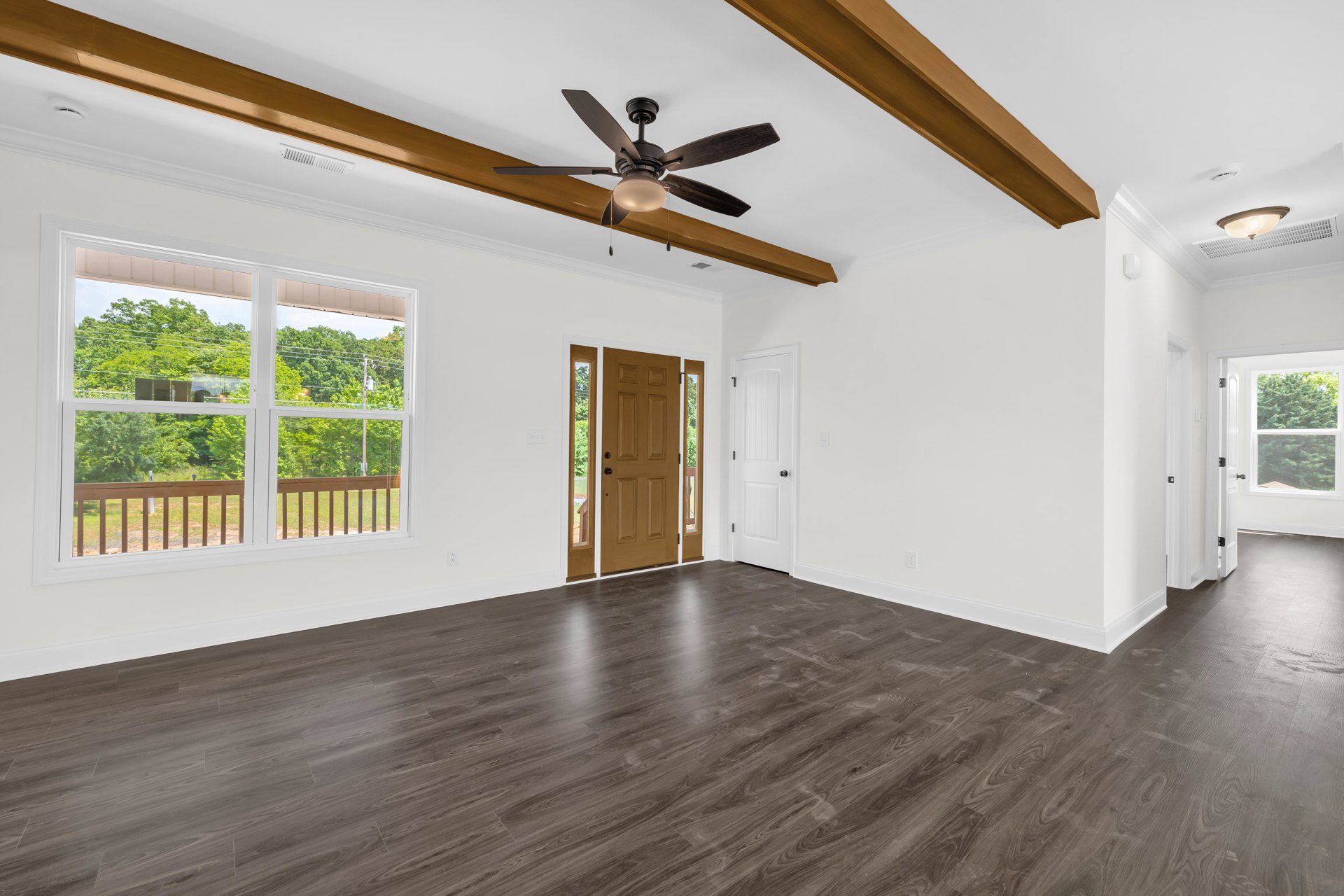Wood flooring and ceiling fan in a bright room with a brown door featuring glass panes, windows showing trees, grass, and a fence outside.