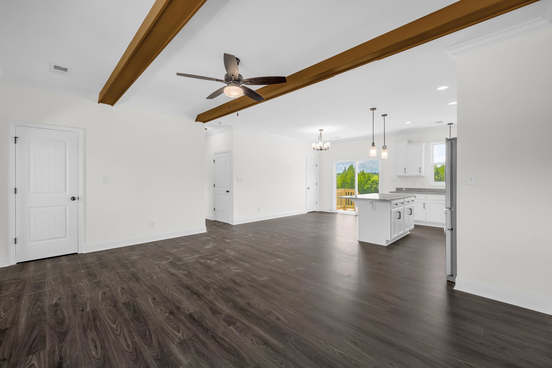 Room with dark wood flooring, white walls, white door with black knob, ceiling fan with light fixture, large window letting in natural light