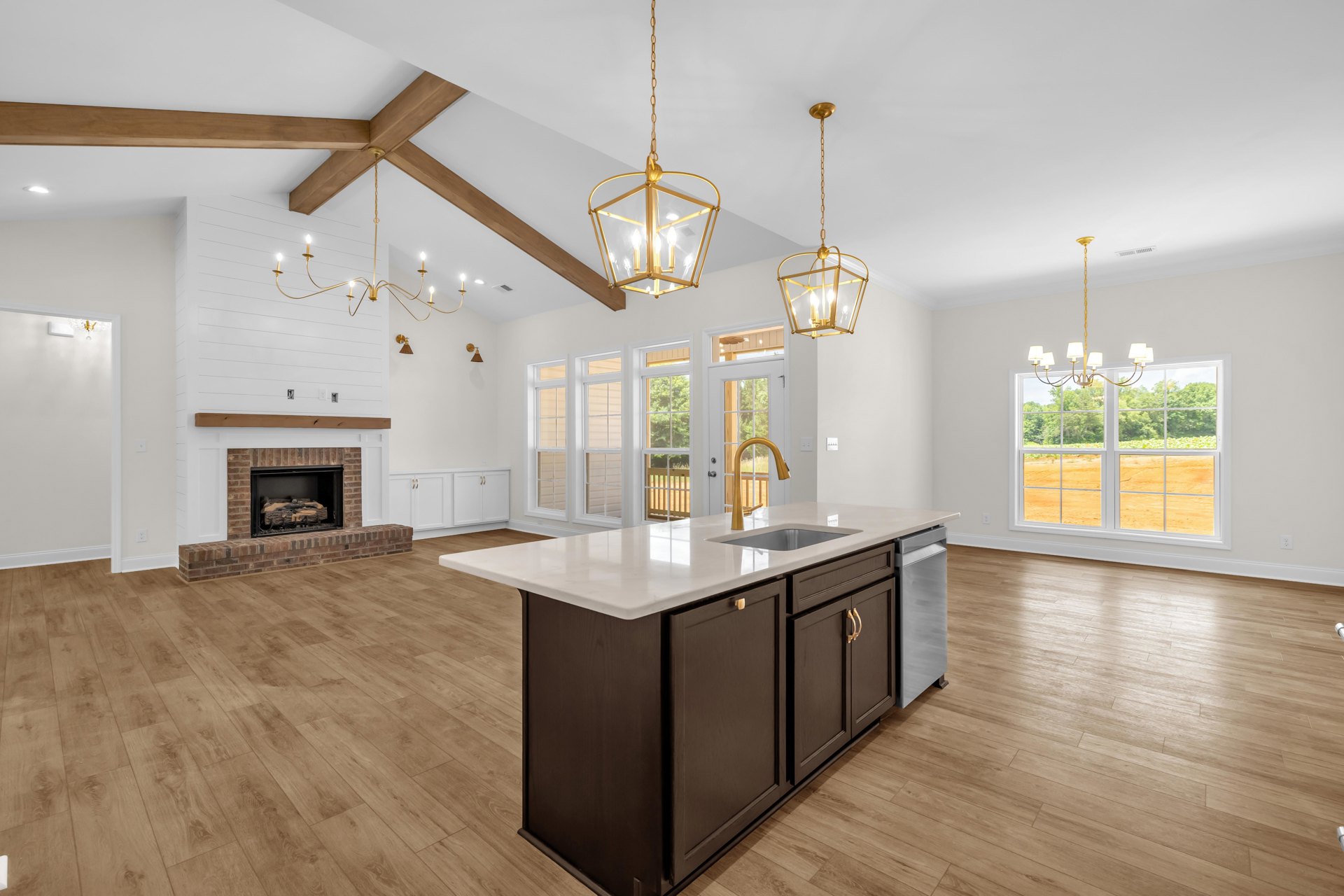 Spacious kitchen featuring a large island with built-in sink, gold chandelier with clear glass above, fireplace with stacked logs, white cabinetry, laminate flooring, and multiple