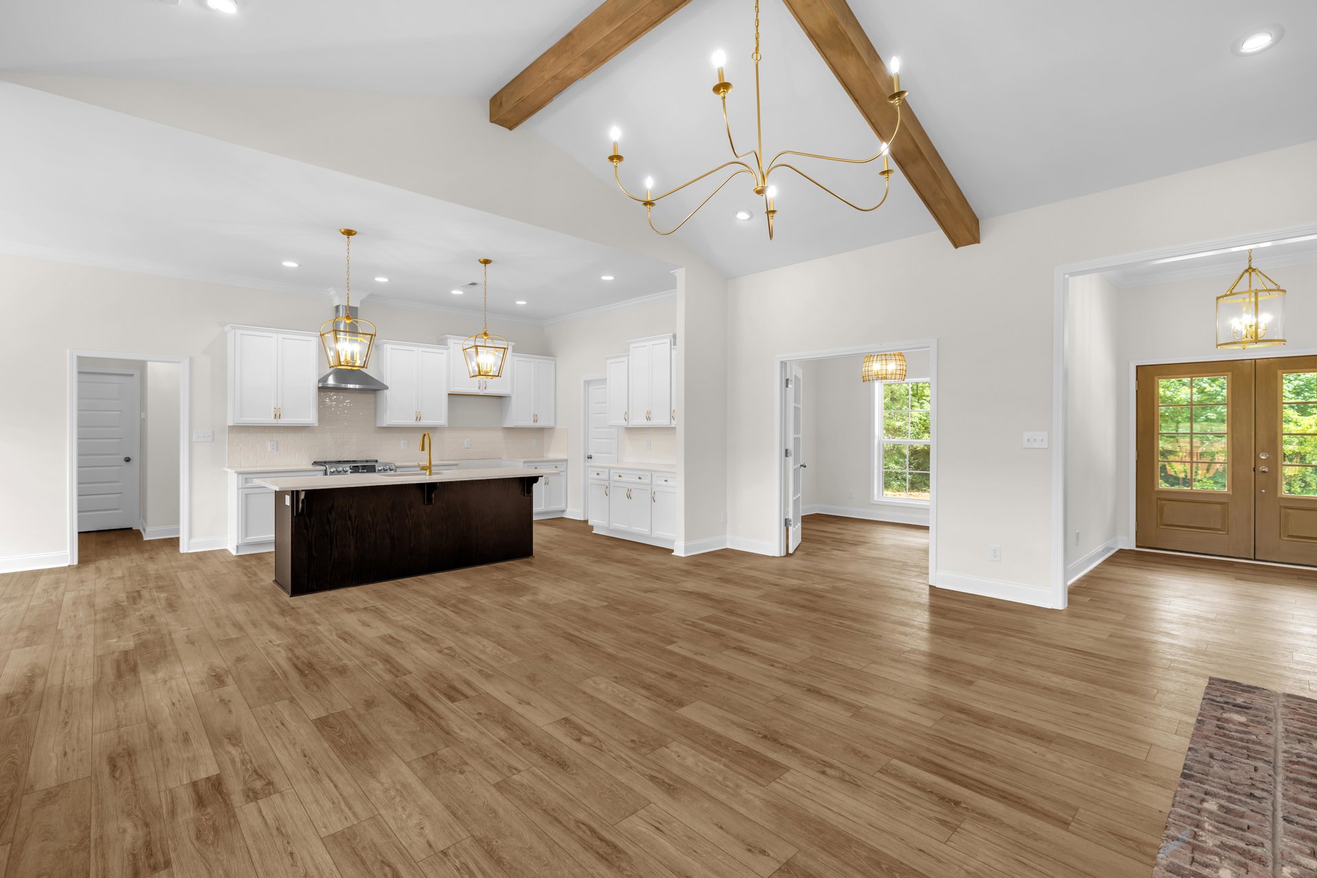 Spacious kitchen and living area with hardwood floors, white walls, central kitchen island featuring sink and stove, double glass-paneled doors, gold chandelier with glass cover