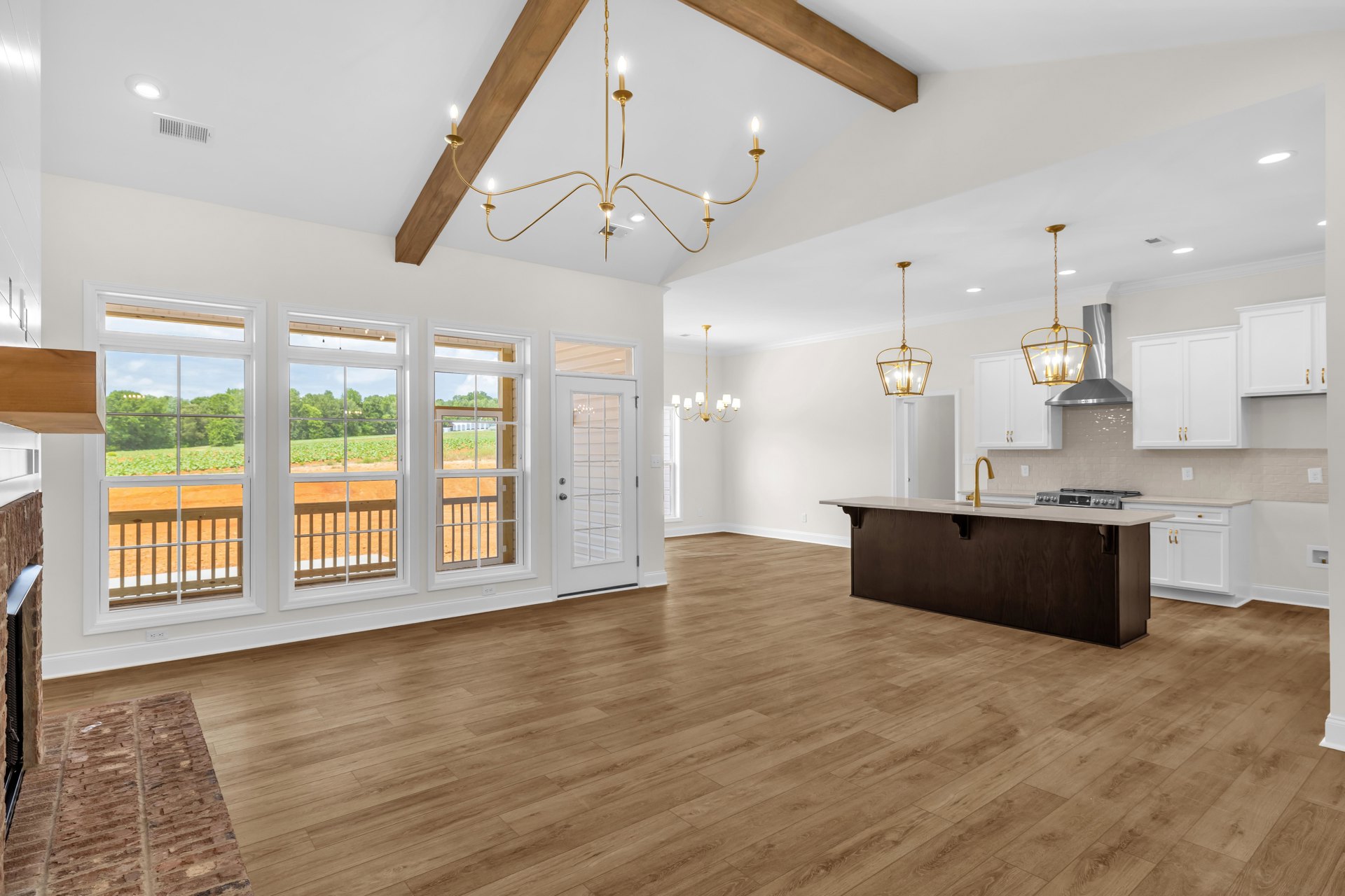Spacious open floor plan featuring hardwood floors, a central kitchen island with white cabinetry, a chandelier hanging from the ceiling, white walls, a kitchen counter with a gold