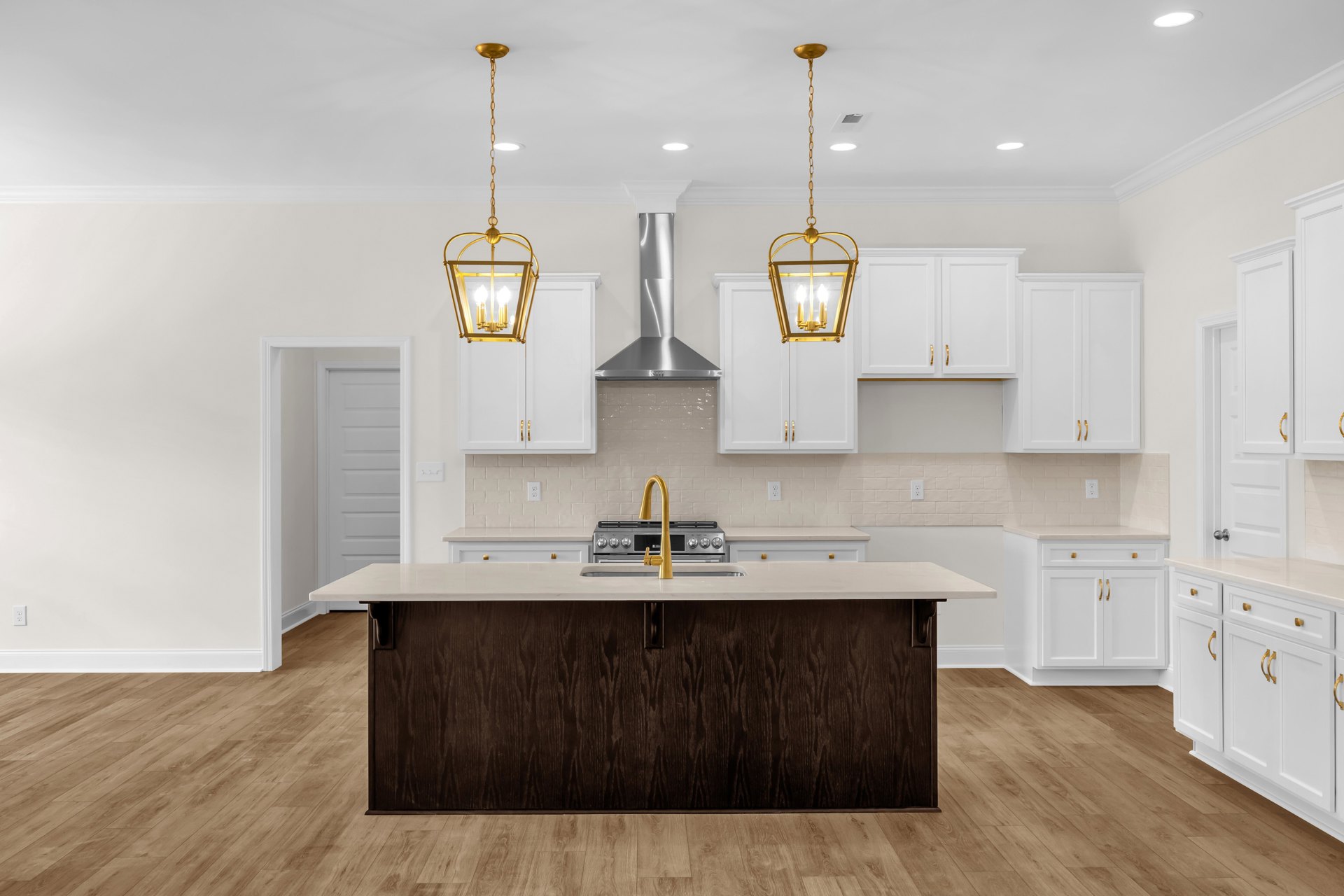 Modern kitchen with white cabinetry, central island featuring a sink and gold faucet, stainless steel stove, gold pendant light fixture, and light countertops