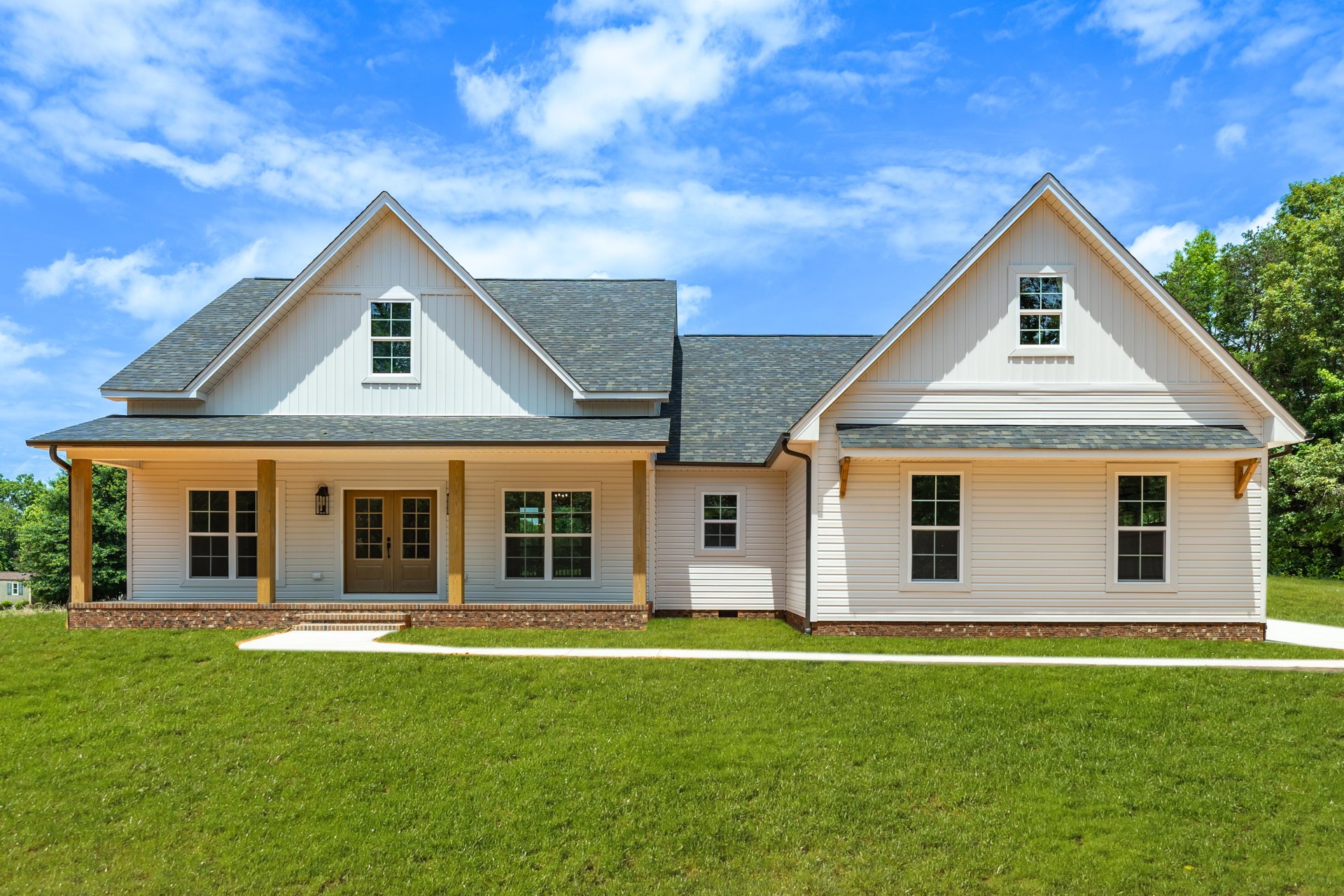 Two-story home with white siding, covered front porch, double glass-paneled doors, white-framed windows, manicured green lawn, and blue sky with scattered clouds