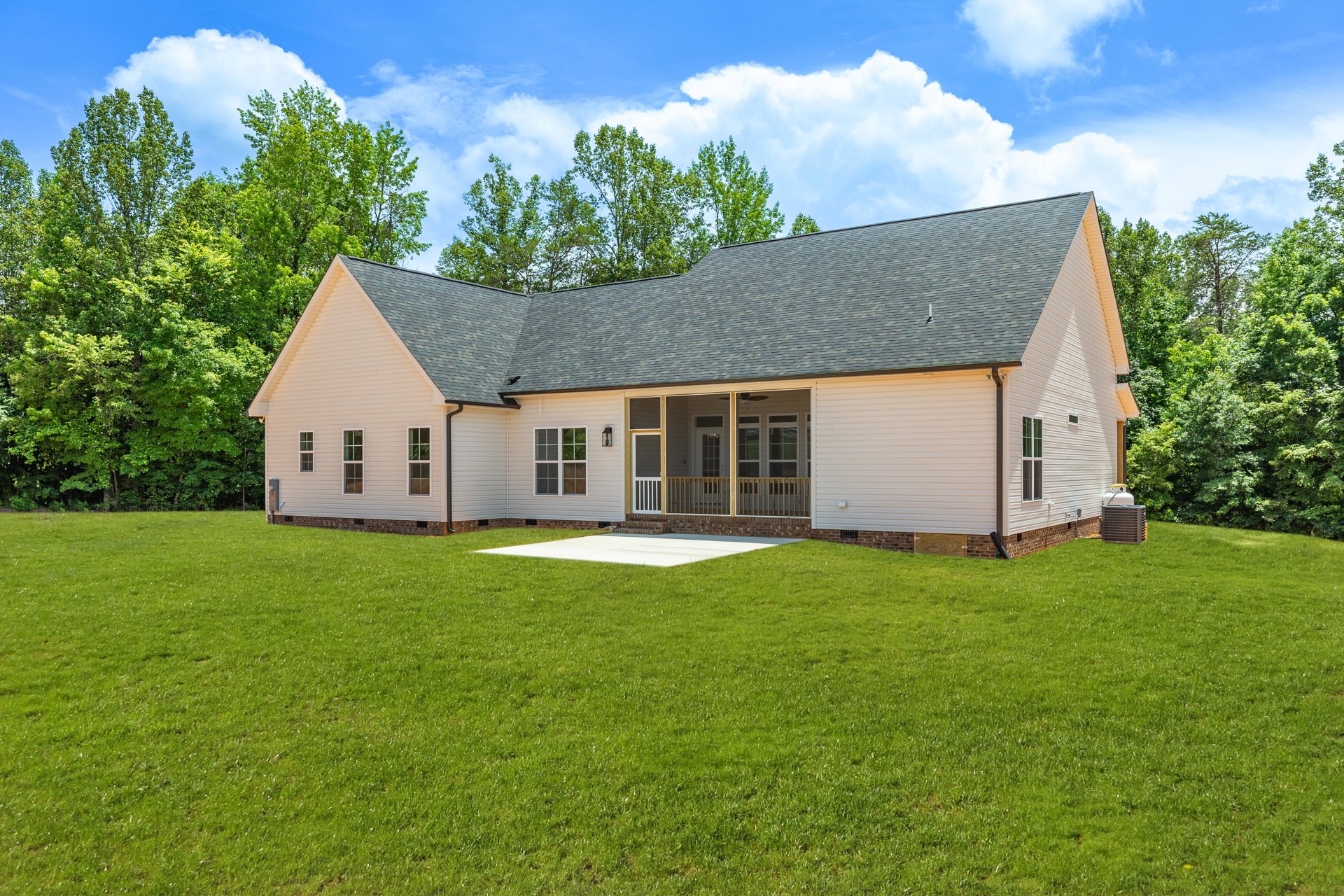 White farmhouse with covered porch, wooden railing, concrete driveway, and manicured lawn bordered by mature trees; Robert Frost Farm visible in the background.
