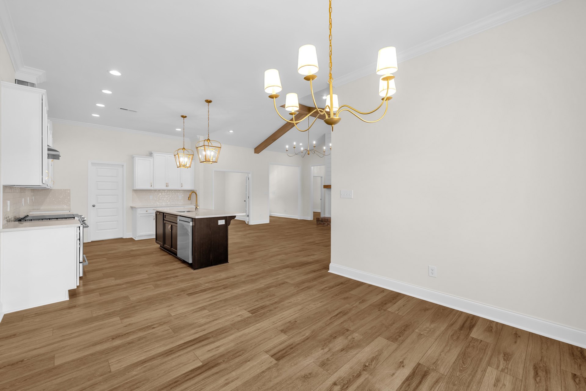 Open kitchen and dining area with wood laminate flooring, white cabinetry, stainless steel dishwasher, and a chandelier hanging from a plaster ceiling.