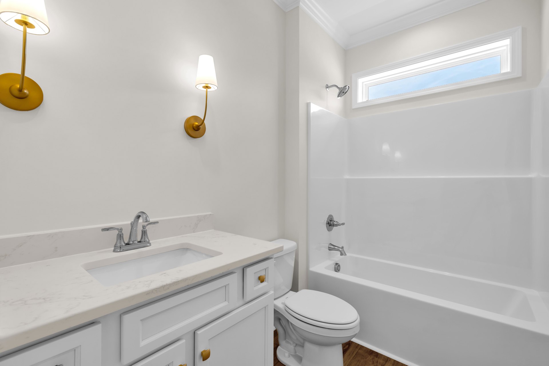 Bathroom with white tile floor, white toilet with lid closed, rectangular window in ceiling, sink with chrome faucet set in cabinetry, wall-mounted lamp with white shade