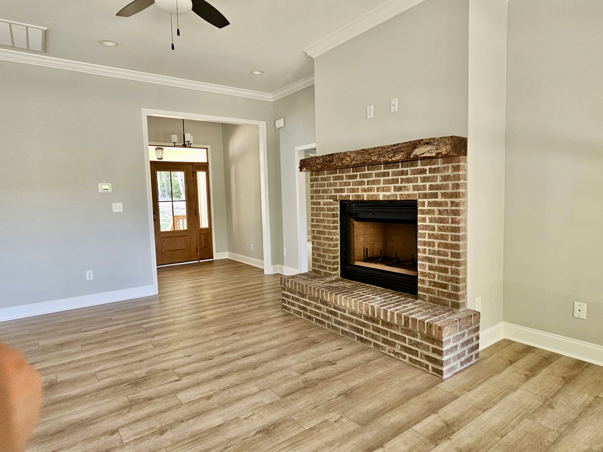 Brick fireplace with black frame set against a white wall, wood flooring, and partial view of a lamp and person's leg in a modern living room.