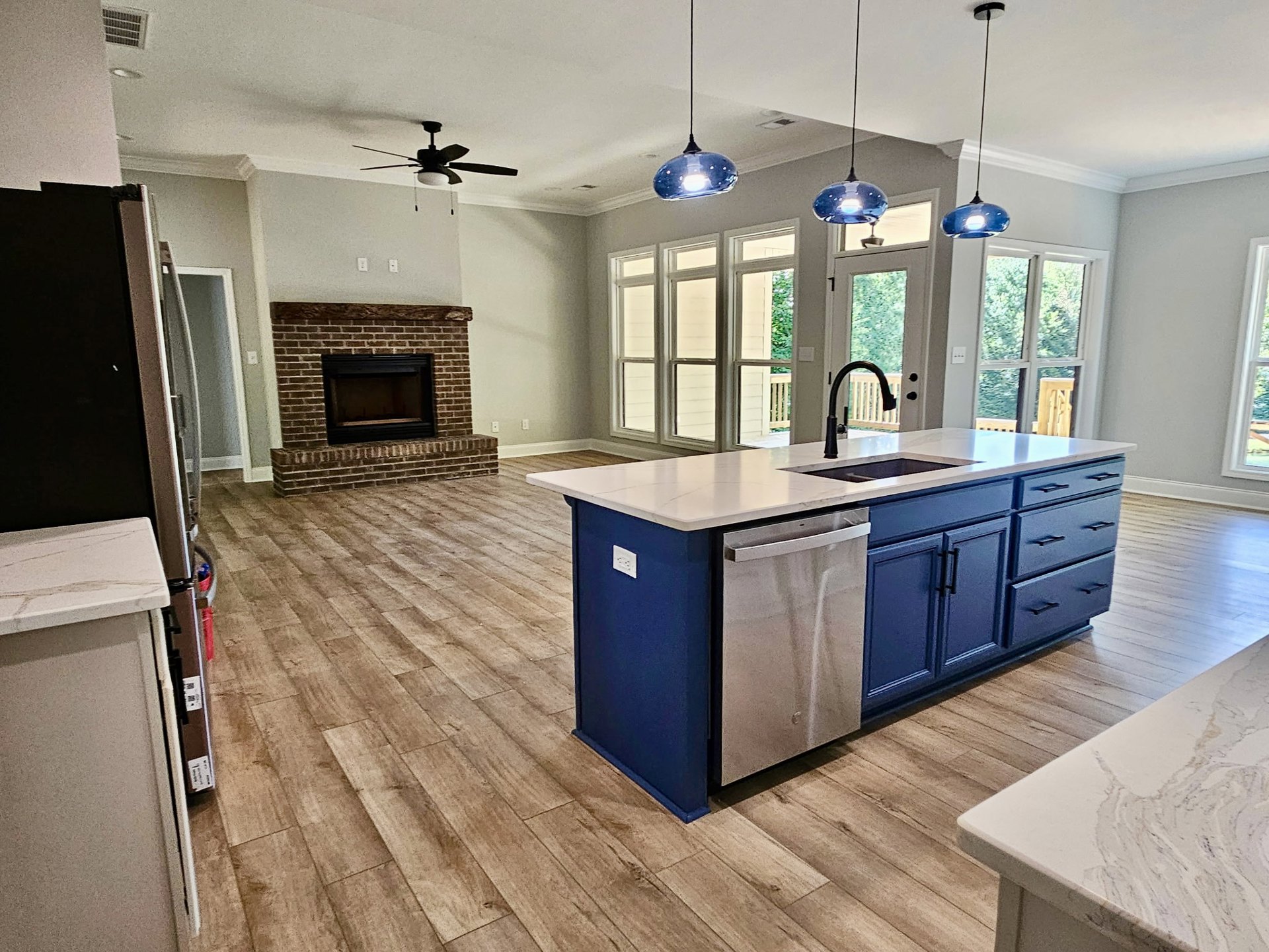Kitchen with brick fireplace, wood flooring, marble countertops, kitchen island with built-in dishwasher, pendant light hanging from wire, cabinetry and drawers, close-up of